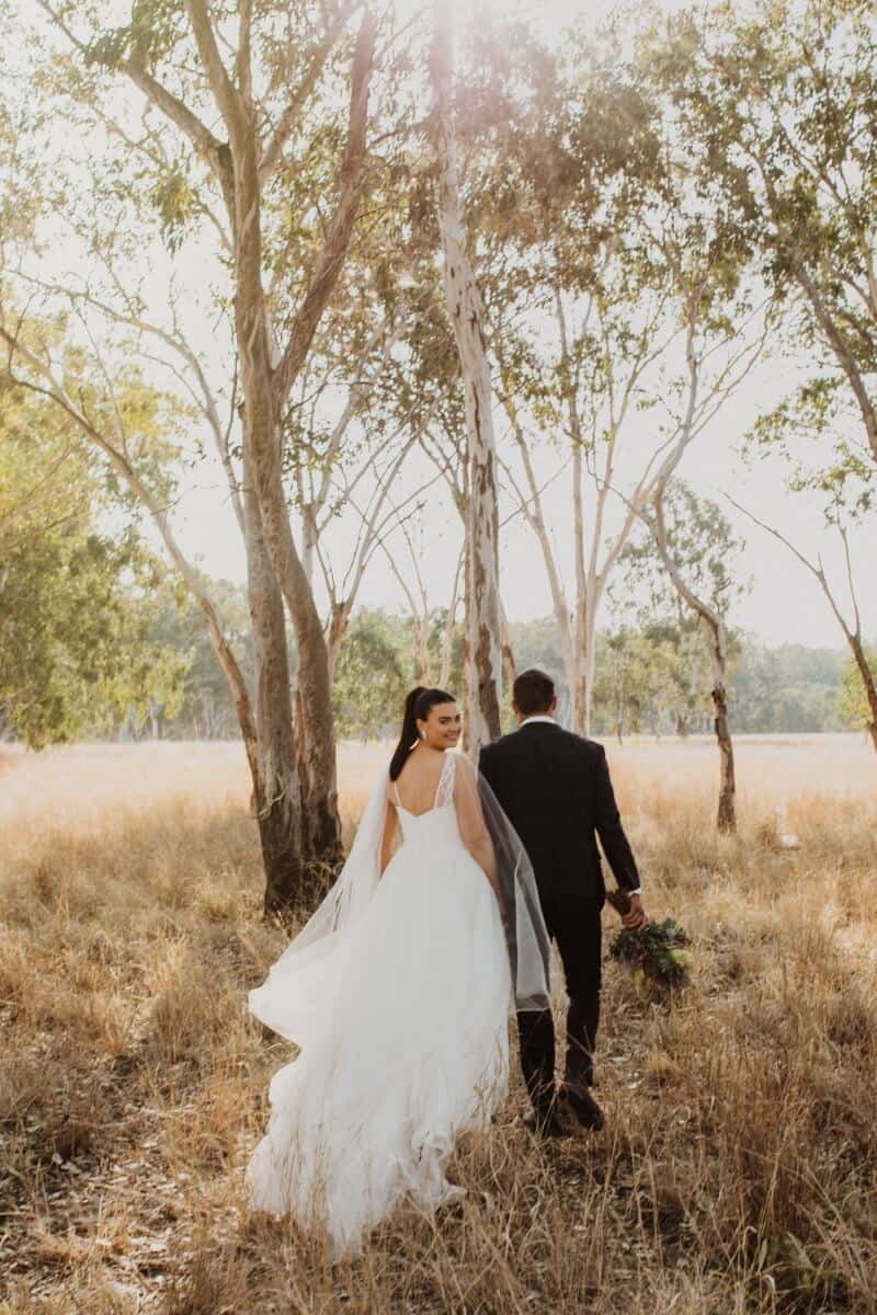 Bride and groom standing in field at sunset