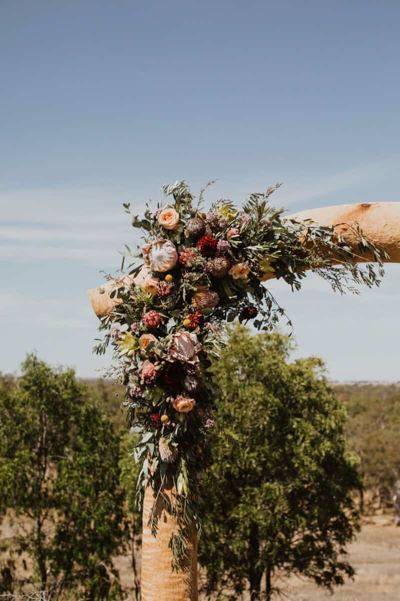 Close up image of floral arrangement by Emily Beutel on wooden archway at wedding ceremony