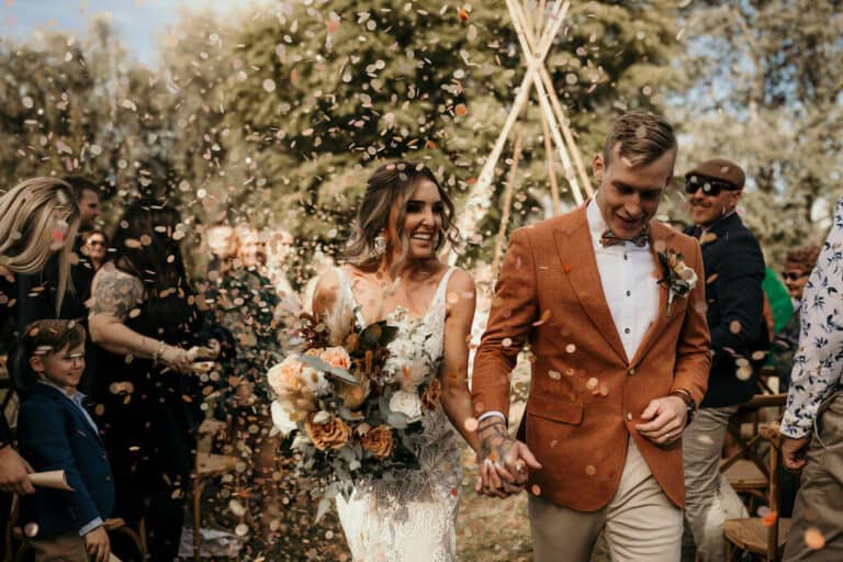 Bride and groom walking down aisle with confetti thrown by guests