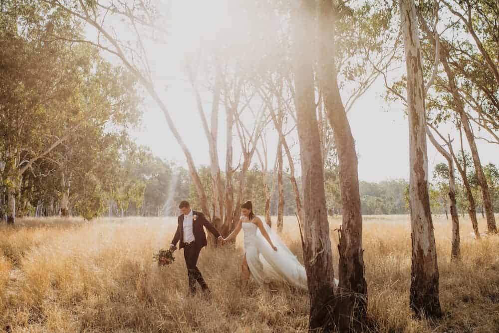 Bride and groom walking through field holding hands
