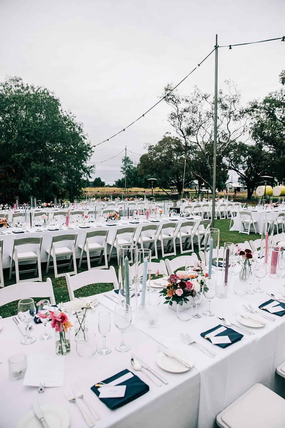 Long tables set up for wedding outside on grass with lanterns hanging above