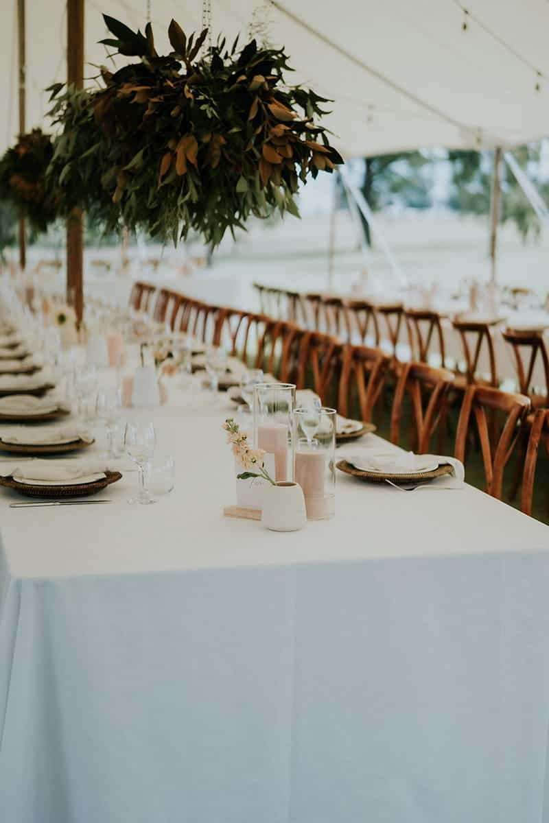 Long tables set for guests at a wedding with floral arrangements hanging from ceiling